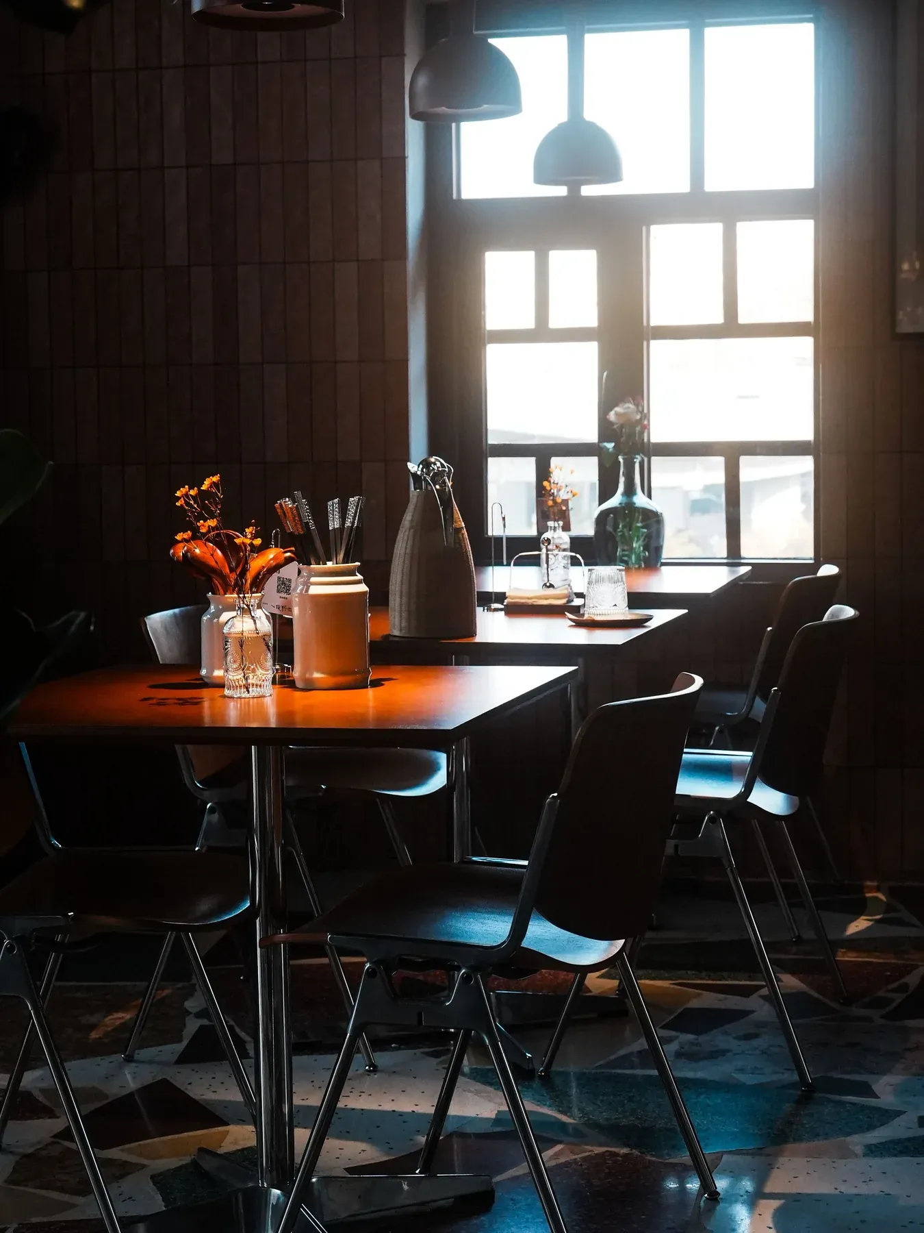 Dark dining tables and black chairs in a warm interior — reference image for the CHASHNI dark-finish dining table
