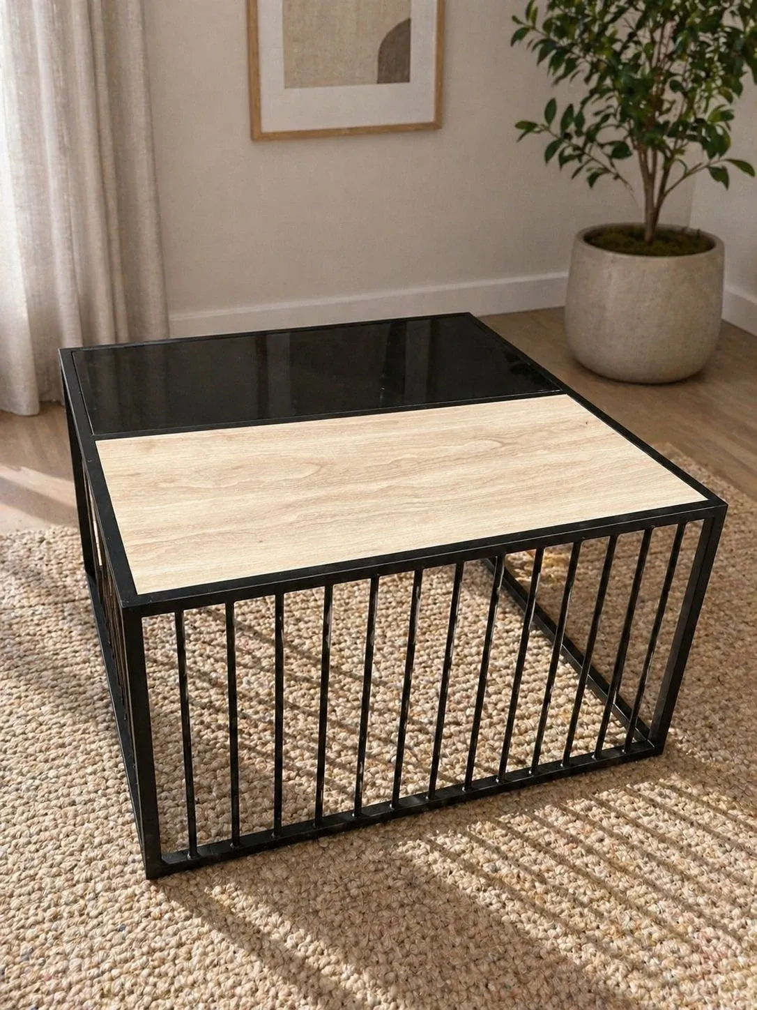 Square coffee table with a black slatted metal base and a top split between light wood-look and dark glass — photograph of the JAALI table