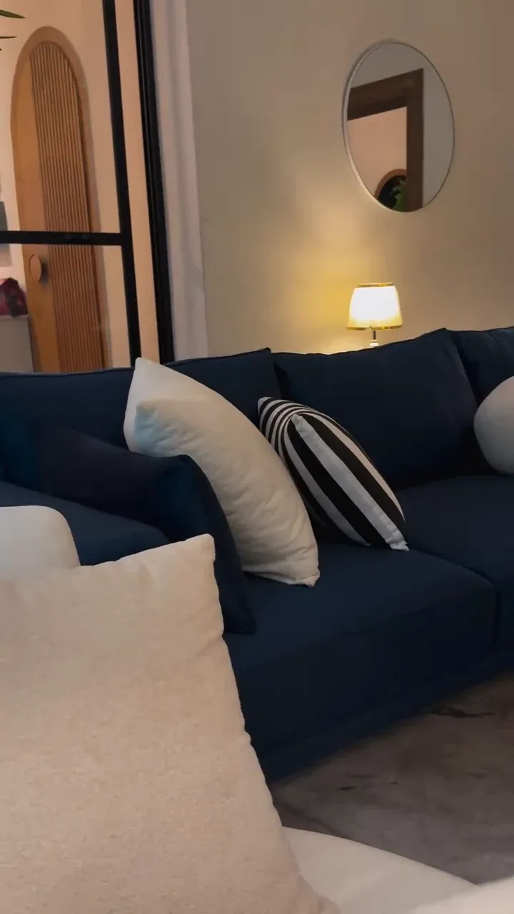 NEELAM deep blue sofa seen from the end, with white and striped scatter cushions along the back